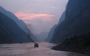 Boat sailing through a misty mountain river at sunset.