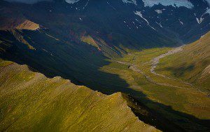 Aerial view of a green valley with a winding river and rugged mountain slopes.