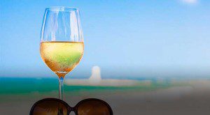 A glass of white wine with a scenic blurred background and sunglasses.