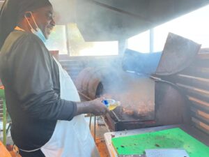 A man grilling meat on a smoky barbecue grill outdoors.