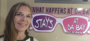 Woman smiling beside humorous sign about "Da Bay.